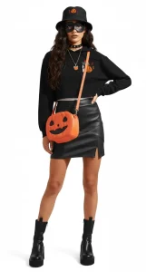 A woman models the FLY Clothing Co. "Midnight Lantern" alternative streetwear outfit, featuring a black cropped hoodie with pumpkin graphics, a black leather mini skirt with a side slit, and chunky black platform boots. She is accessorized with a black pumpkin-embroidered bucket hat, a black eye mask, a black choker, a pumpkin pendant necklace, and a round orange jack-o'-lantern crossbody bag.