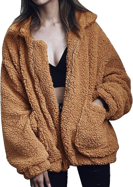 A woman wearing a tan, oversized shaggy faux-fur teddy jacket with a full-zip front, large lapel collar, and deep side pockets.