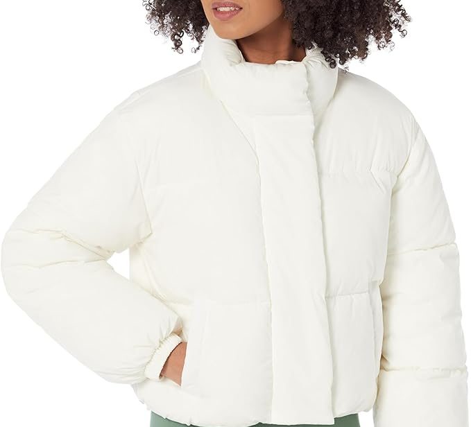 A woman wearing a crisp white, cropped full-zip puffer jacket with a high stand-up collar, quilted paneling, and elasticized cuffs, paired with sage green leggings