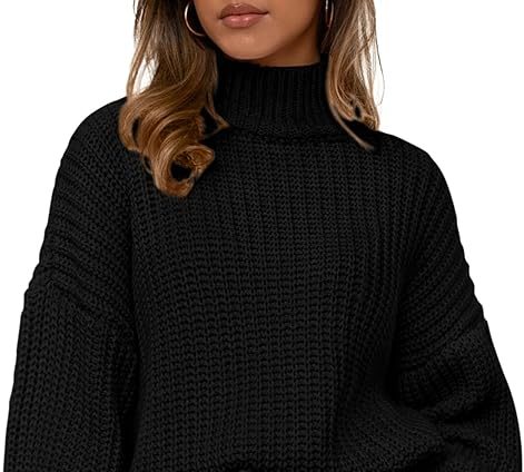 A woman wearing a black, oversized, chunky knit turtleneck sweater with long, loose sleeves and ribbed cuffs and hem