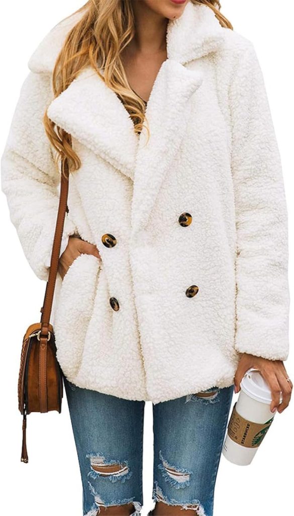 A woman wearing a white, double-breasted sherpa fleece coat with a wide notched lapel, four dark tortoiseshell buttons, and side pockets.