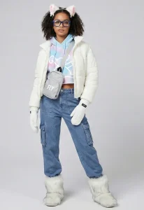 A woman models the FLY Clothing Co. "Arctic Fluff" winter outfit featuring a white cropped puffer jacket over a blue and pink tie-dye hoodie and blue denim cargo pants. She is wearing oversized white faux-fur boots, white cat ears with pink interiors, blue-framed glasses, and a grey crossbody bag with "FLY" branding.