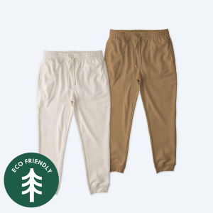 Two pairs of Stanley Stella Unisex Flyer Joggers in Natural Raw and Desert Dust colors, featuring a green "Eco Friendly" tree logo, elastic waistbands with drawstrings, and ribbed cuffs.