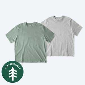 Two blank Stanley Stella unisex Freestyler heavyweight t-shirts, one in a muted sage green and one in heather grey, displayed on a clean white background with a green "Eco Friendly" tree icon for custom apparel design services.