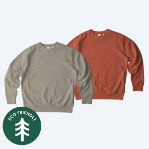 Two eco-friendly custom Stanley/Stella Unisex Changer 2.0 Crewneck Sweatshirts in an earthy olive green and a vibrant burnt orange, featuring an "Eco-Friendly" seal, part of Fly Clothing Co’s sustainable design service in LA and NYC.