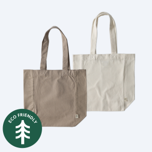 Two blank recycled cotton tote bags, one in a natural ecru cream and one in a soft taupe brown, displayed on a clean white background with a green "Eco Friendly" tree icon for custom branding design services.