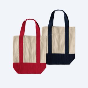 Two blank two-tone cotton grocery tote bags, one in natural tan with vibrant red accents and one in natural tan with classic navy blue accents, displayed on a clean white background for custom branding design services.